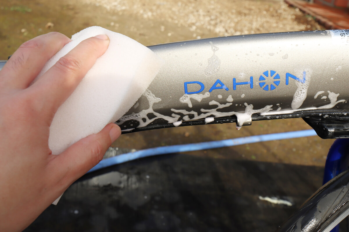 自転車フレームを白いスポンジで洗う